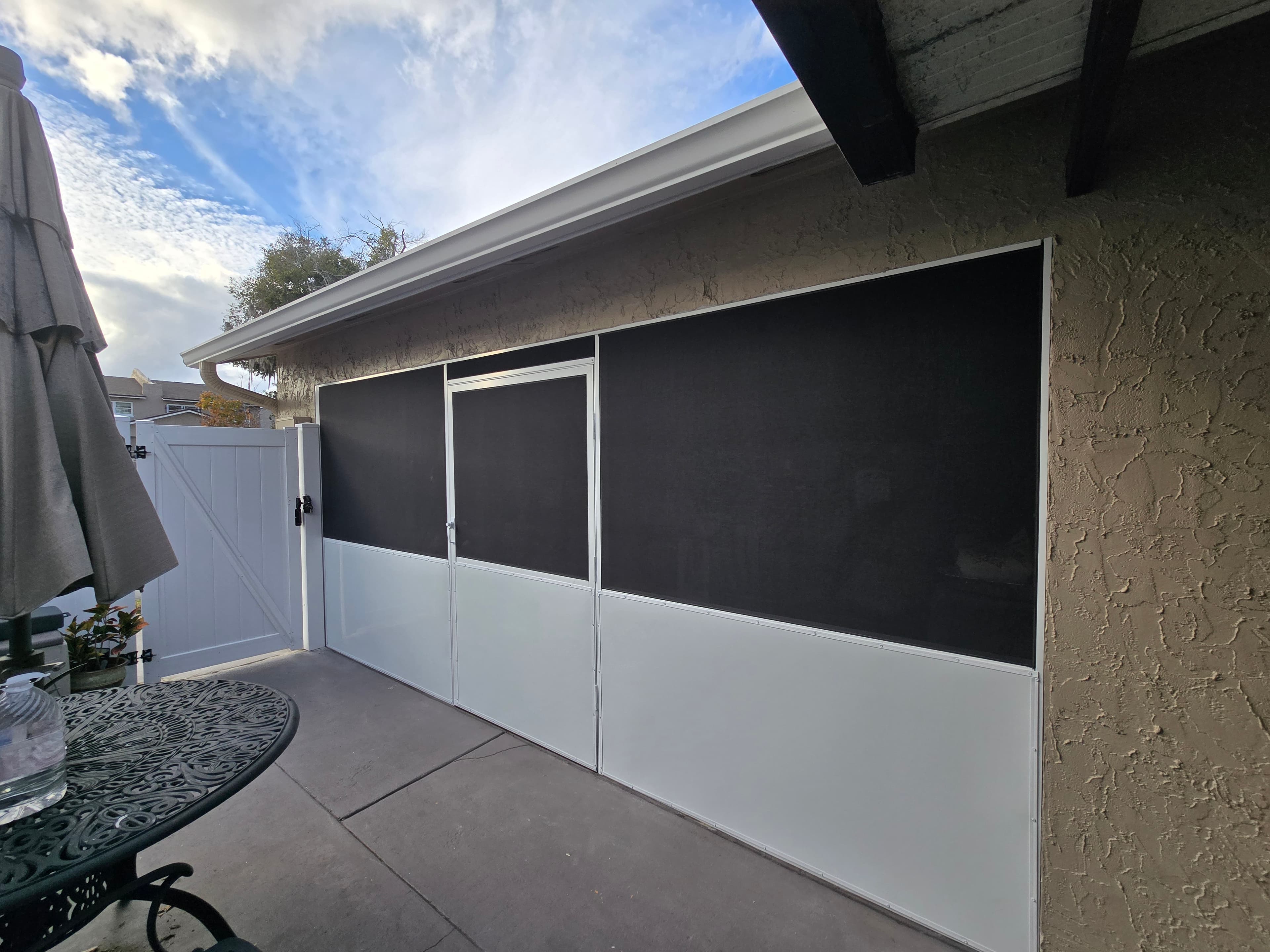 Patio enclosure with black mesh screens and white lower panels next to a white gate.