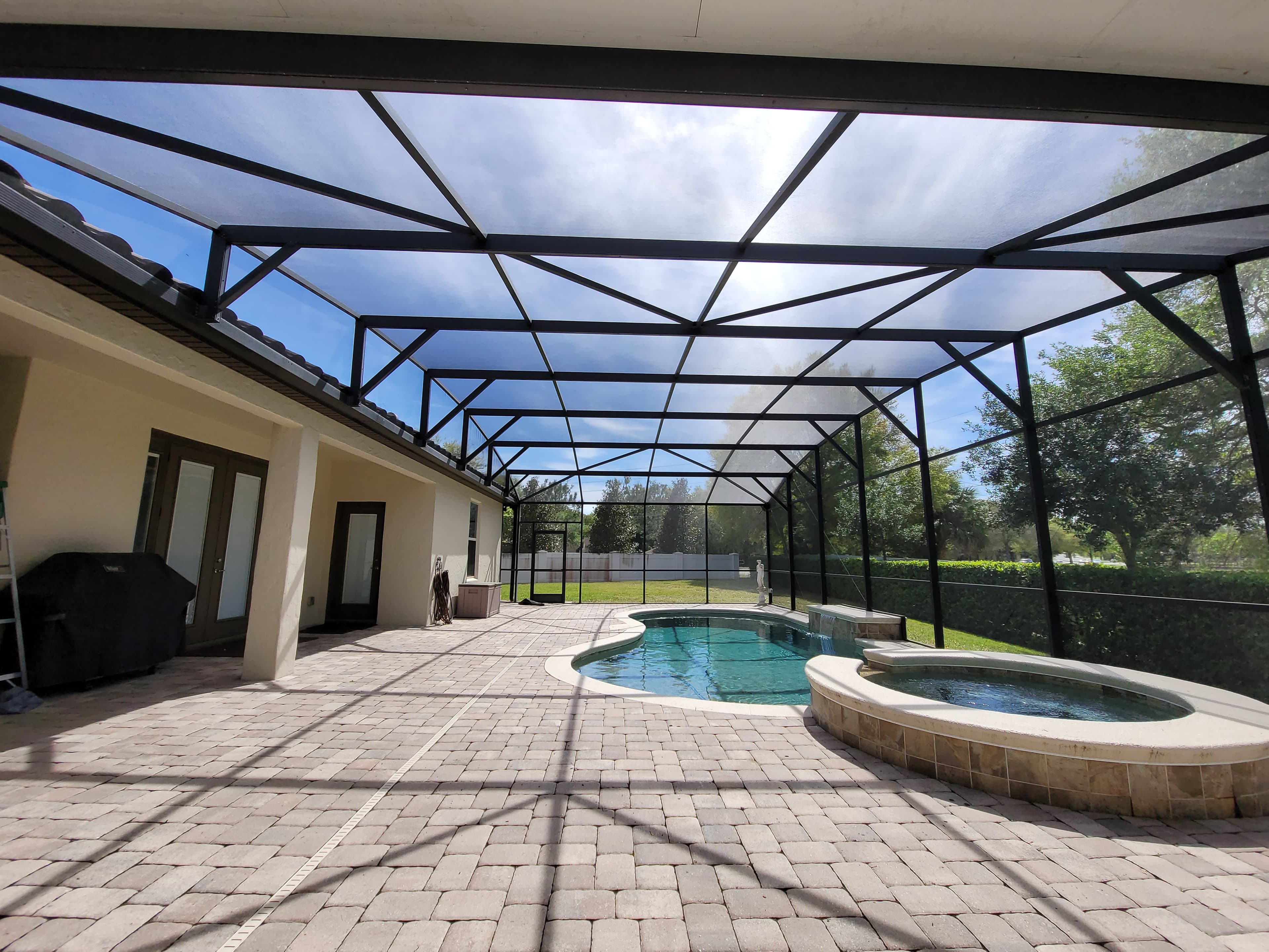 Screened-in backyard patio featuring a swimming pool and hot tub surrounded by brick pavers.