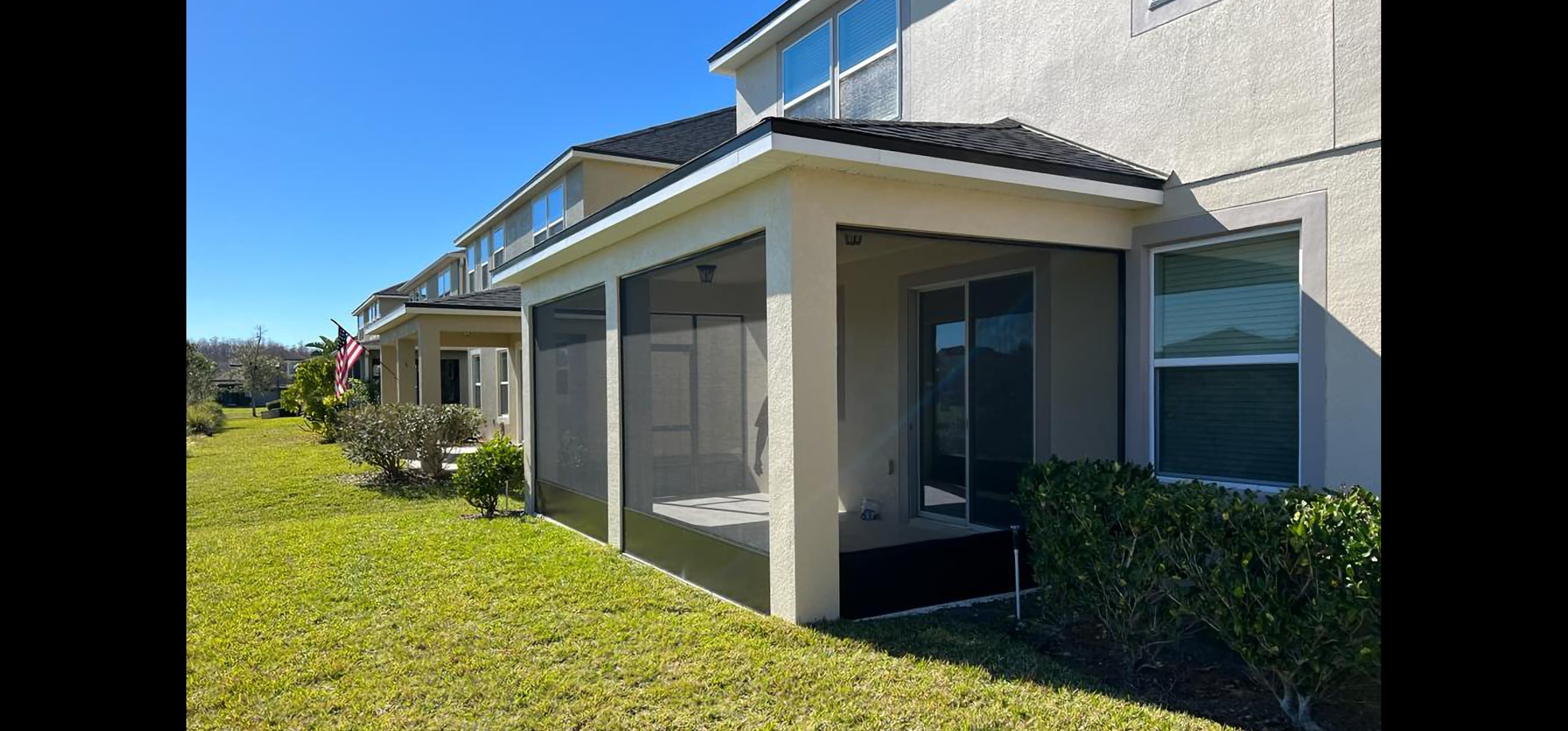 Large screened-in patio with black mesh panels attached to a beige house on sunny day.